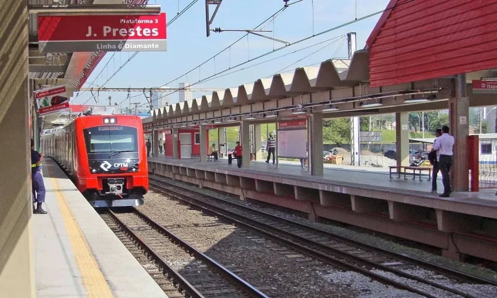 Estação ferroviária na Região Metropolitana de São Paulo, com trem em aproximação e fluxo de passageiros na plataforma.