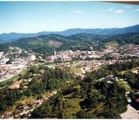 Vista aérea de Brusque SC, com skyline urbano cercado por morros verdes.