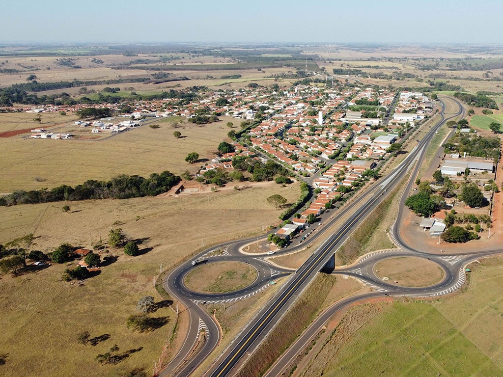 Vista aérea de uma cidade pequena com áreas urbanas e plantações ao fundo; rodovias e rotatórias ao centro