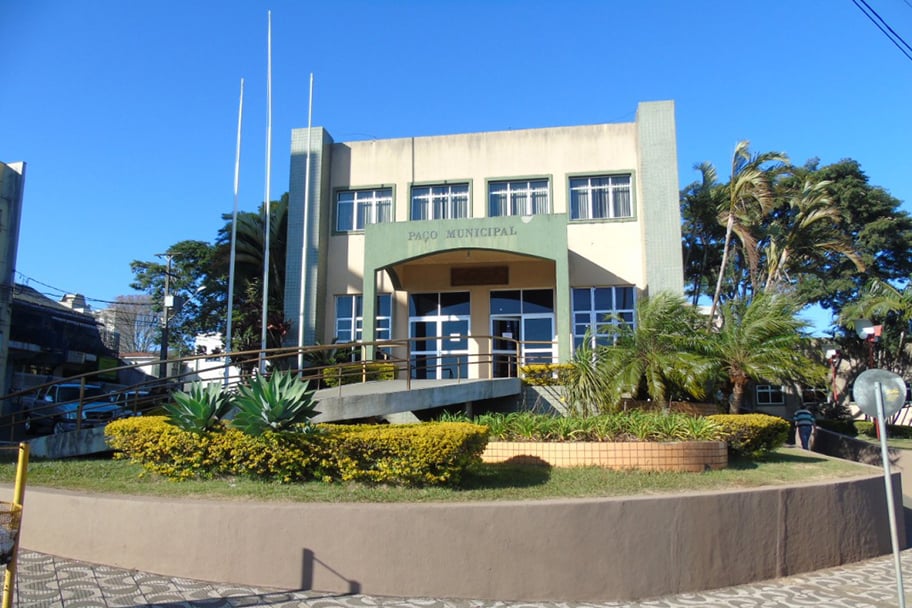 Fachada de uma sede de prefeitura municipal no Sul do Brasil, com bandeiras e praça arborizada
