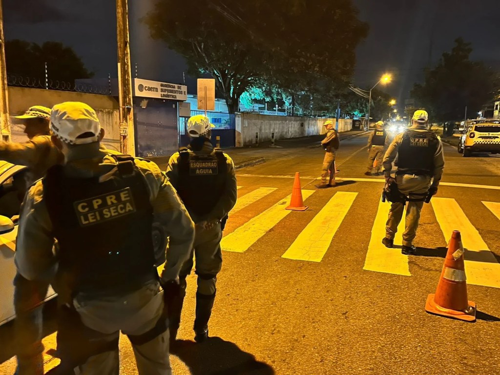 Agentes de fiscalização em operação urbana, com cones e viaturas ao fundo