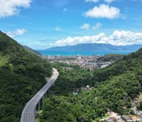 Vista aérea da orla de Caraguatatuba, com vegetação, cidade e mar ao fundo, em dia claro