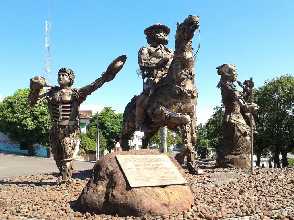 Escultura urbana em Crissiumal RS, com figuras históricas em metal; ao fundo, área urbana da cidade