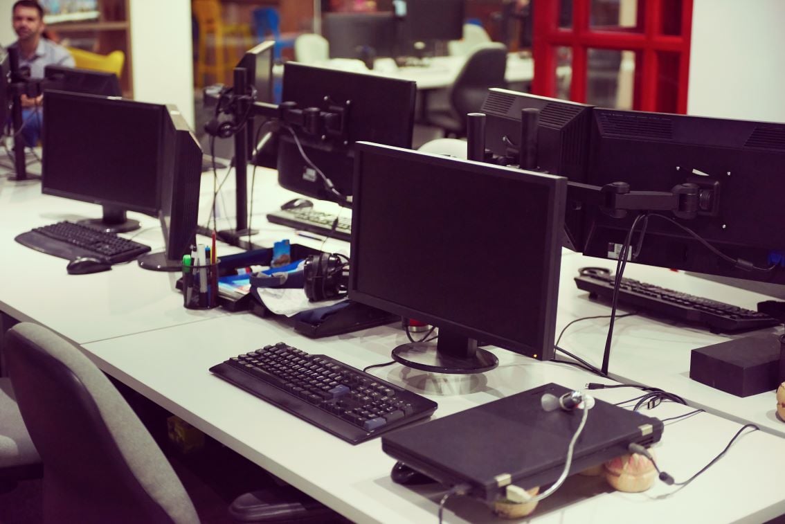 Laboratório de informática educacional, com bancadas, computadores e estudantes ao fundo