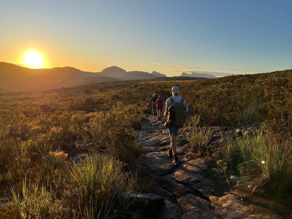 Trilha em vegetação de Caatinga, com dois caminhantes ao pôr do sol