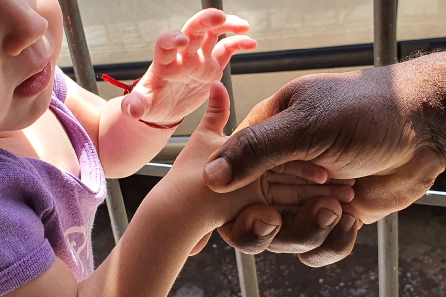 Mãos de uma criança e de um adulto se tocando, em gesto de cuidado em ambiente institucional, representando acolhimento e proteção