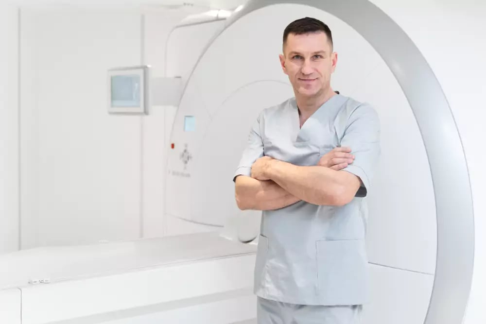 Profissional de Radiologia em ambiente hospitalar, ao lado de equipamento de imagem