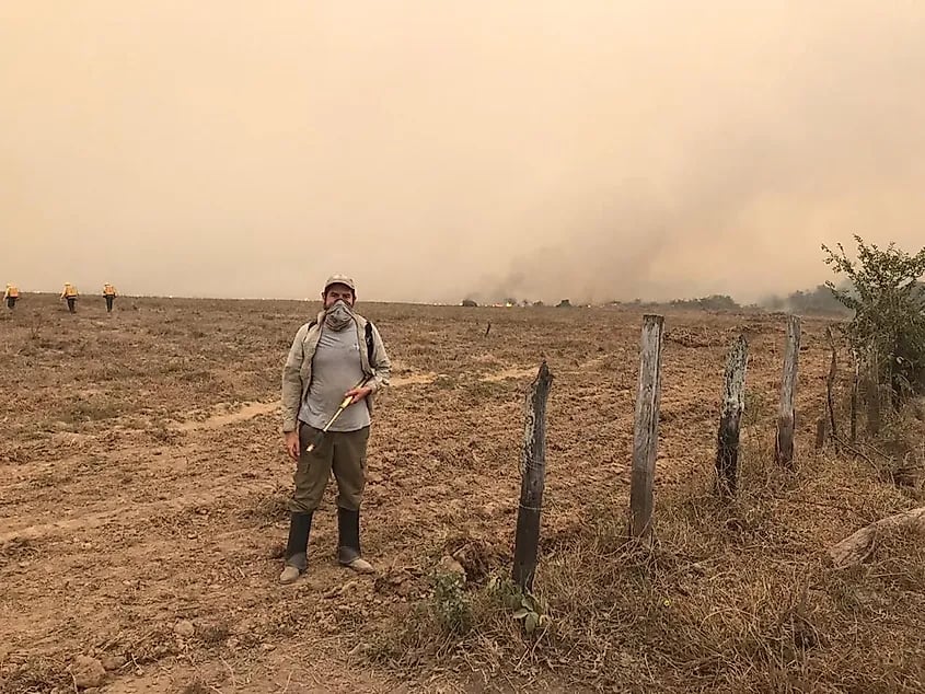 Brigadistas de incêndio usando ferramentas em campo aberto, com fumaça ao fundo