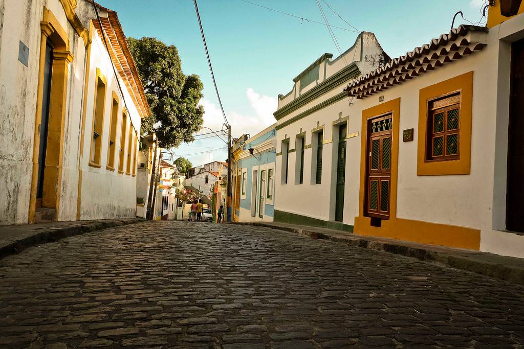 Paisagem urbana do interior de Pernambuco, com casario colorido e rua de pedra sob céu ensolarado