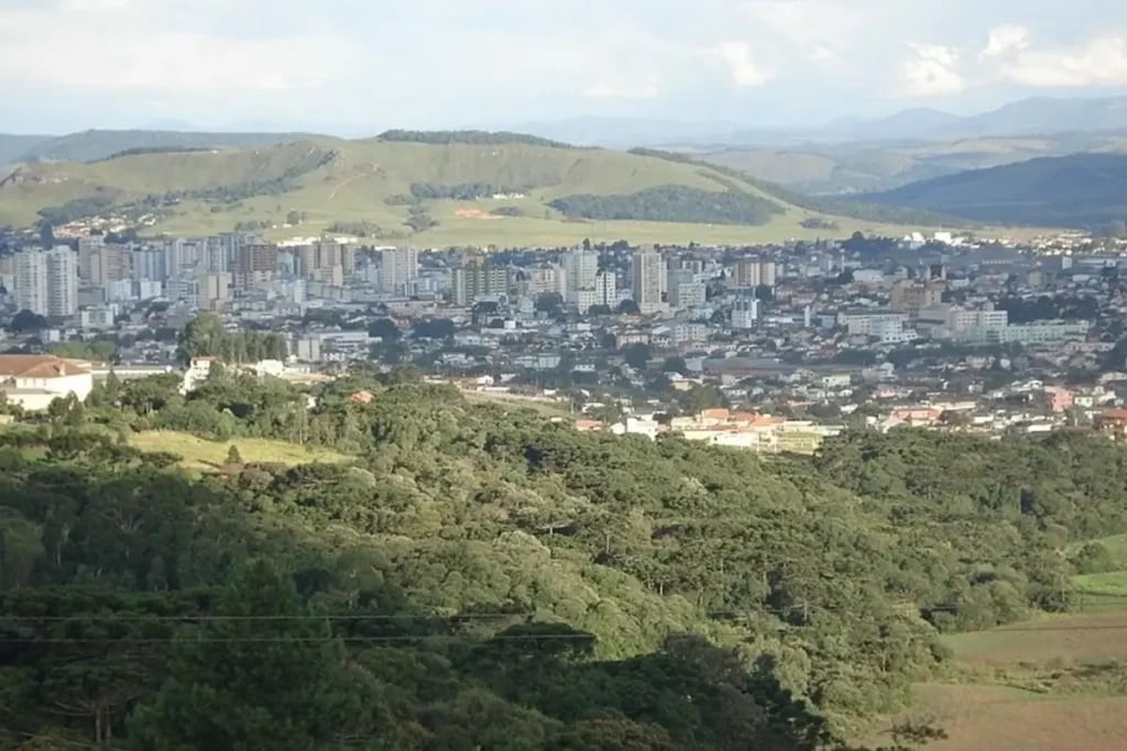 Vista urbana de Lages SC, com prédios e morros ao fundo, em luz natural
