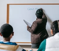 Sala de aula do ensino médio com professor(a) em quadro branco, ambiente moderno e iluminado.