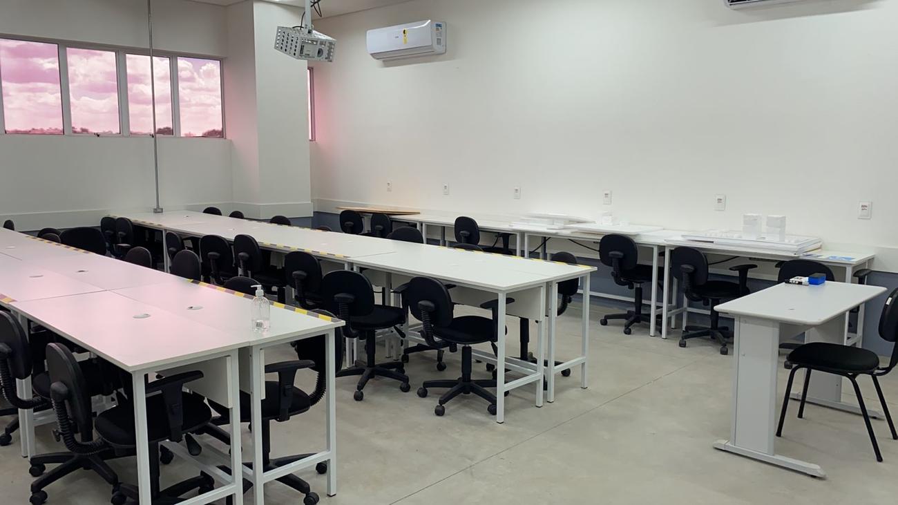 Sala de aula moderna, com mesas, cadeiras e projetor, remetendo a ambiente de aula didática