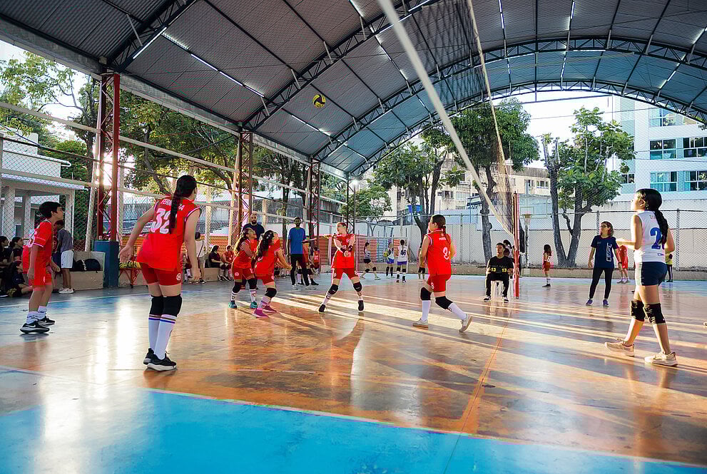 Quadra esportiva universitária com alunos jogando vôlei em ambiente acadêmico moderno e iluminado por luz natural