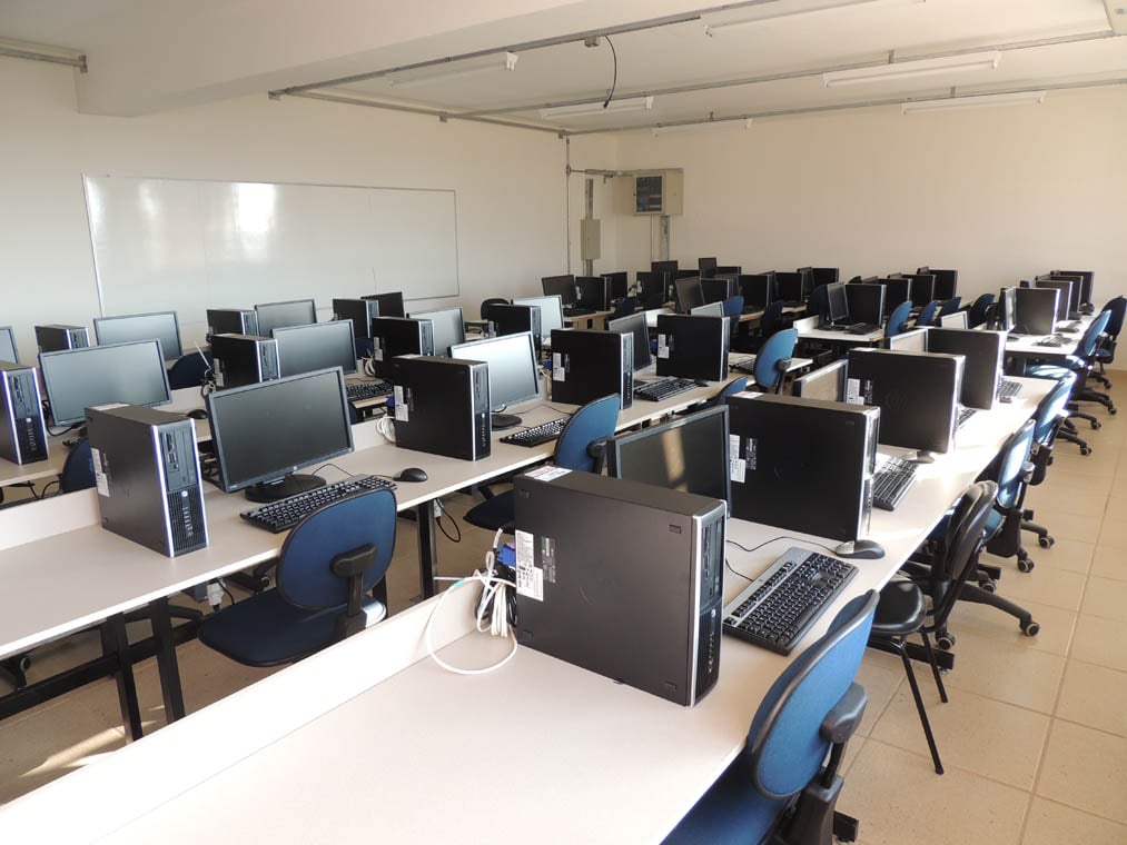 Laboratório de computação em ambiente acadêmico, com mesas e computadores dispostos para atividades práticas em grupo
