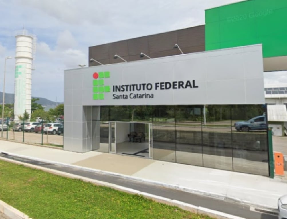 Foto da fachada do Instituto Federal em Santa Catarina, com um ambiente bem iluminado e carros estacionados.
