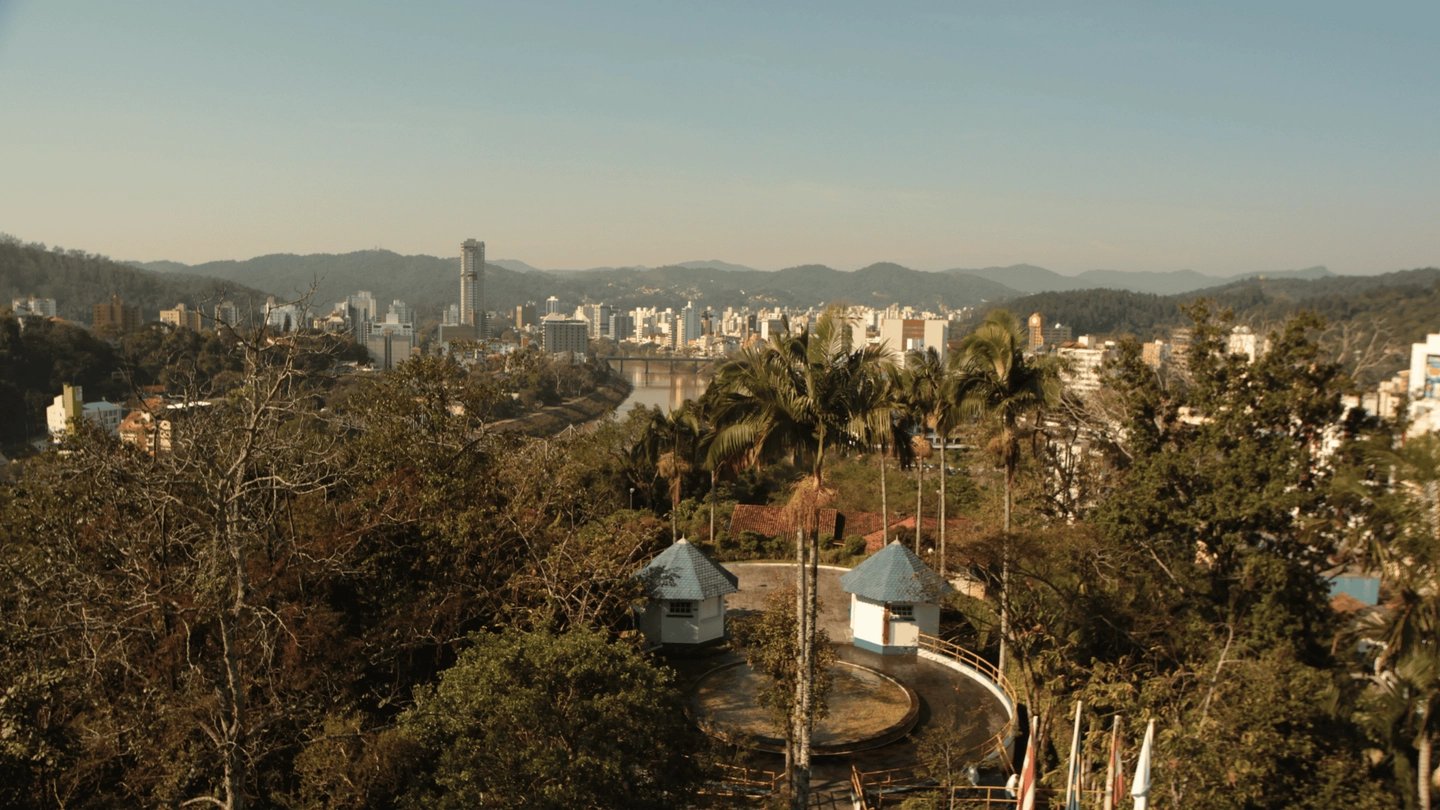 Vista urbana de cidade catarinense, com áreas verdes e morros ao fundo