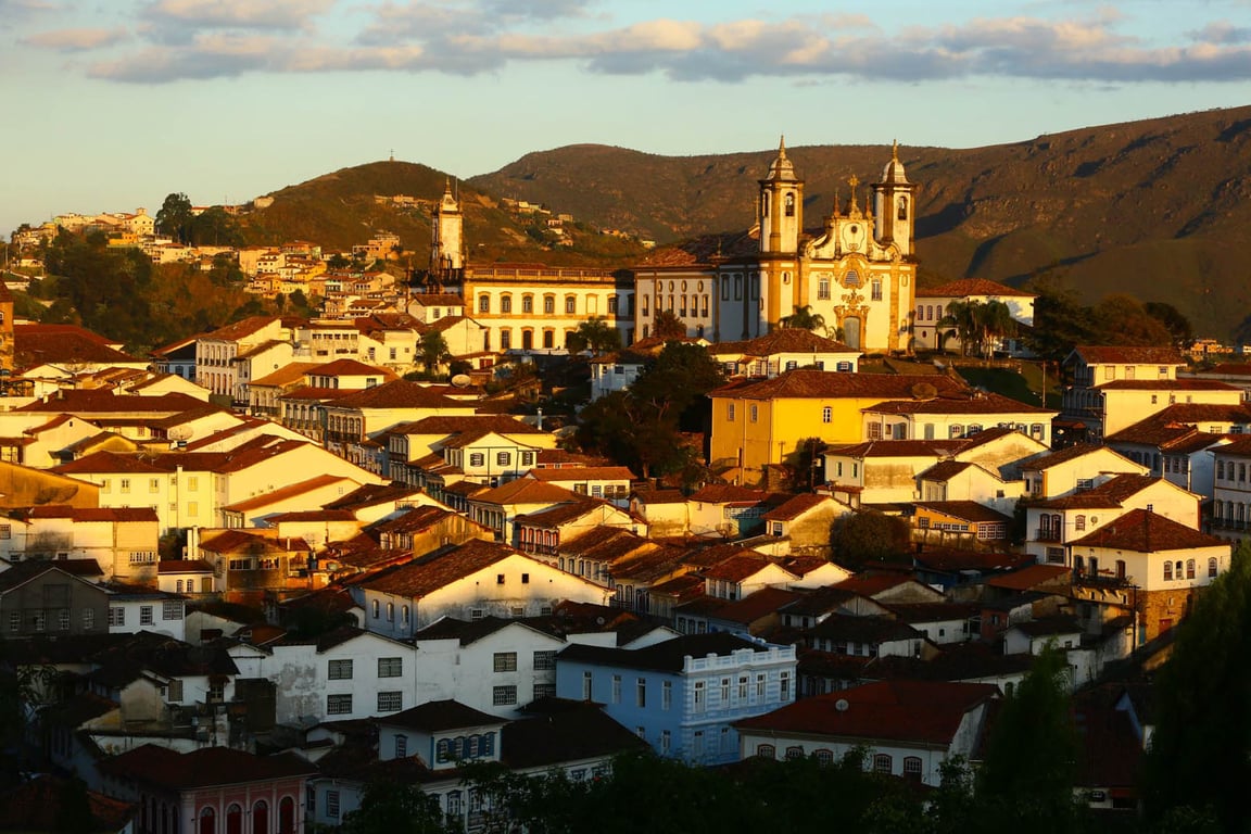 Paisagem de Ouro Preto ao pôr do sol, com igrejas coloniais e morros ao fundo