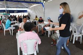 Profissionais de saúde em ação comunitária em área urbana, com EPIs leves e pranchetas, em atividade de orientação