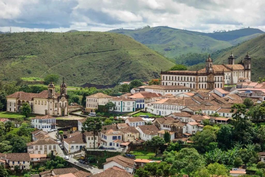 Paisagem urbana em Minas Gerais, com morros ao fundo e prédios baixos, em fim de tarde