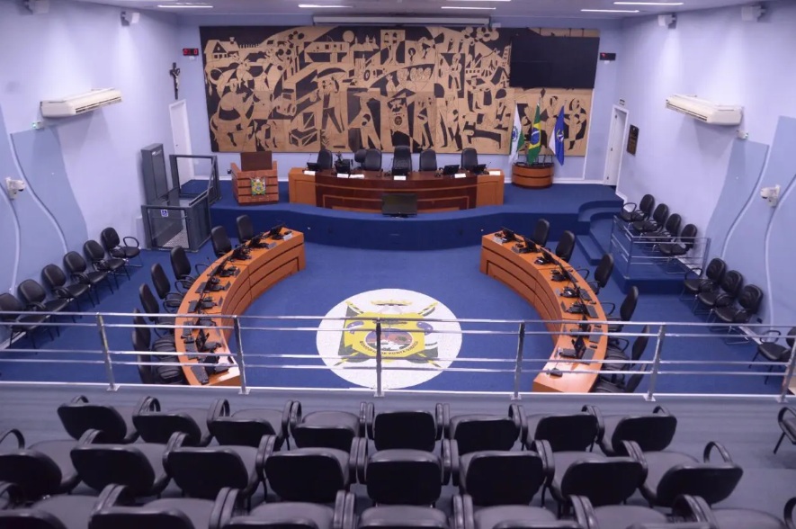 Plenário de câmara municipal brasileira, com bancadas e microfones