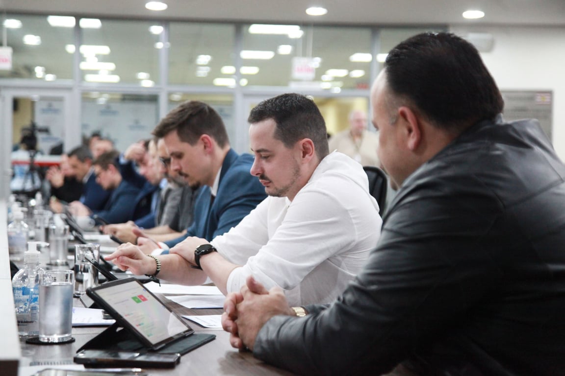 Reunião administrativa, com mesa, papéis e notebooks, em ambiente de gestão pública
