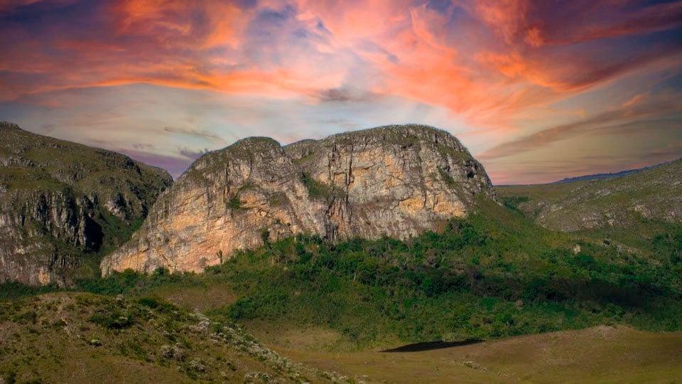 Vista panorâmica da Serra do Cipó, com morros e campos rupestres sob céu azul no fim da tarde