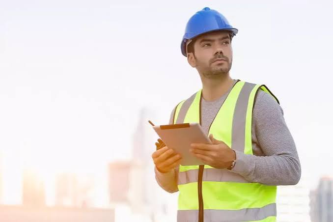Profissional de segurança do trabalho com capacete e prancheta em ambiente industrial
