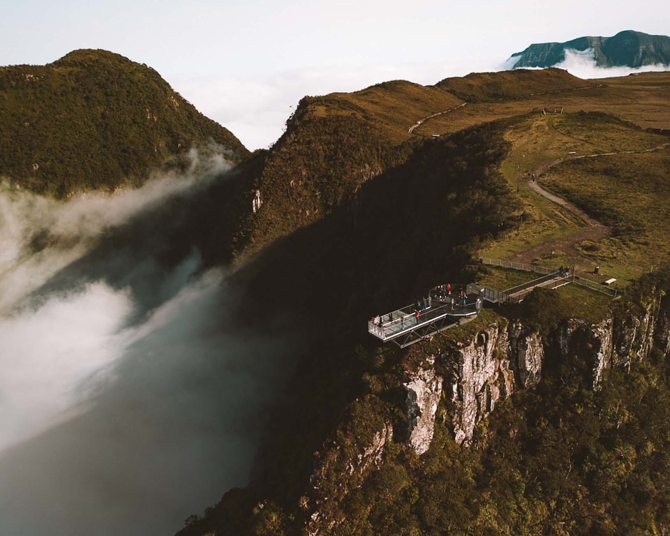 Paisagem de morros verdes ao pôr do sol, com mirante e céu nublado ao fundo