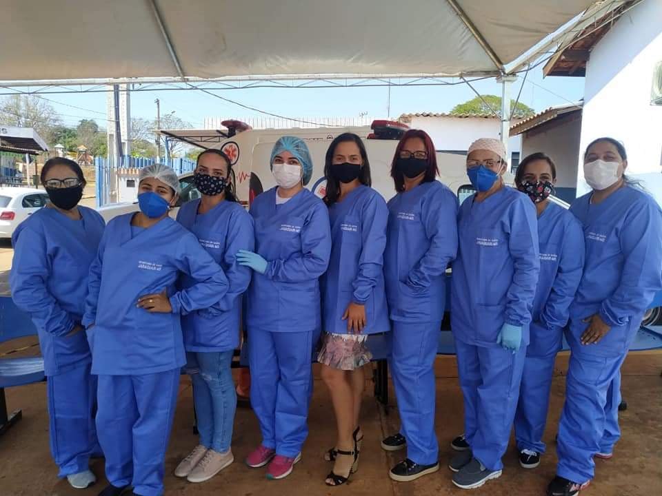 Profissionais de saúde em frente a uma unidade básica de saúde, em ambiente institucional