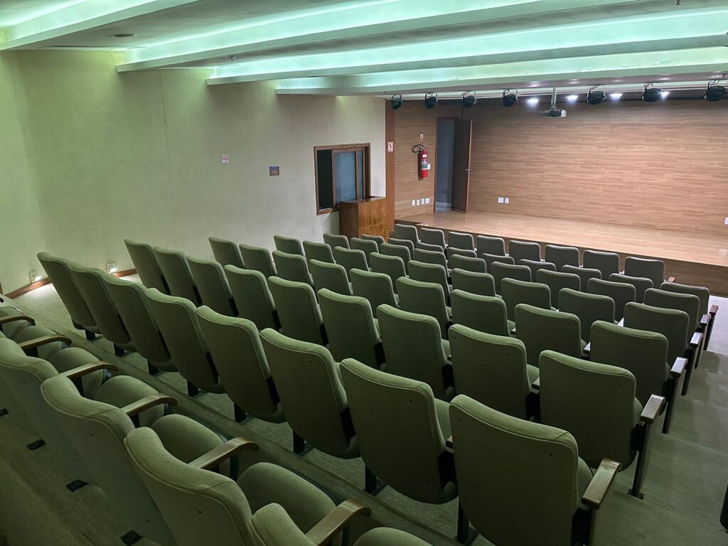 Auditório acadêmico preparado para apresentações, com cadeiras e palco ao fundo