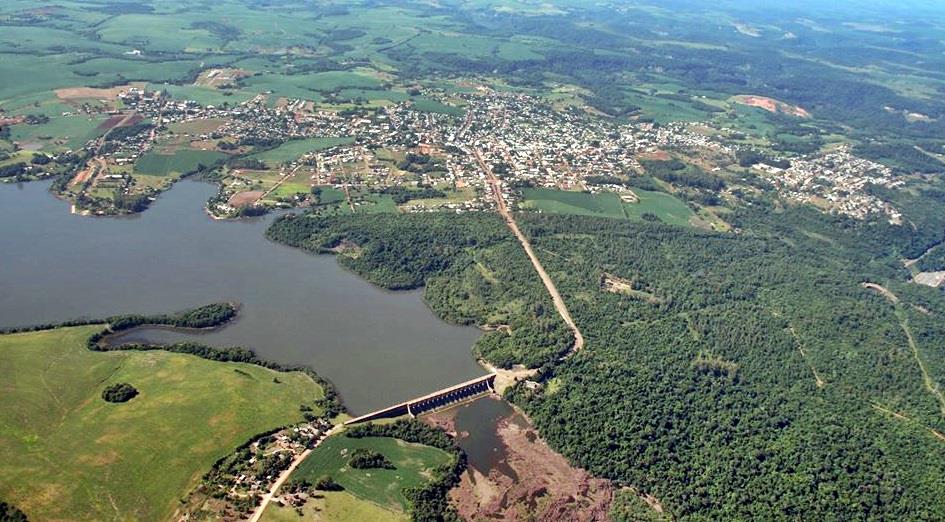 Vista aérea de Salto do Jacuí, mostrando a cidade, a represa e a vegetação ao redor, durante o dia.