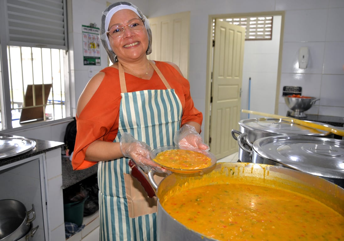 Cozinha de escola com servidora preparando merenda em bancadas de inox, ilustração do trabalho do Serviçal II