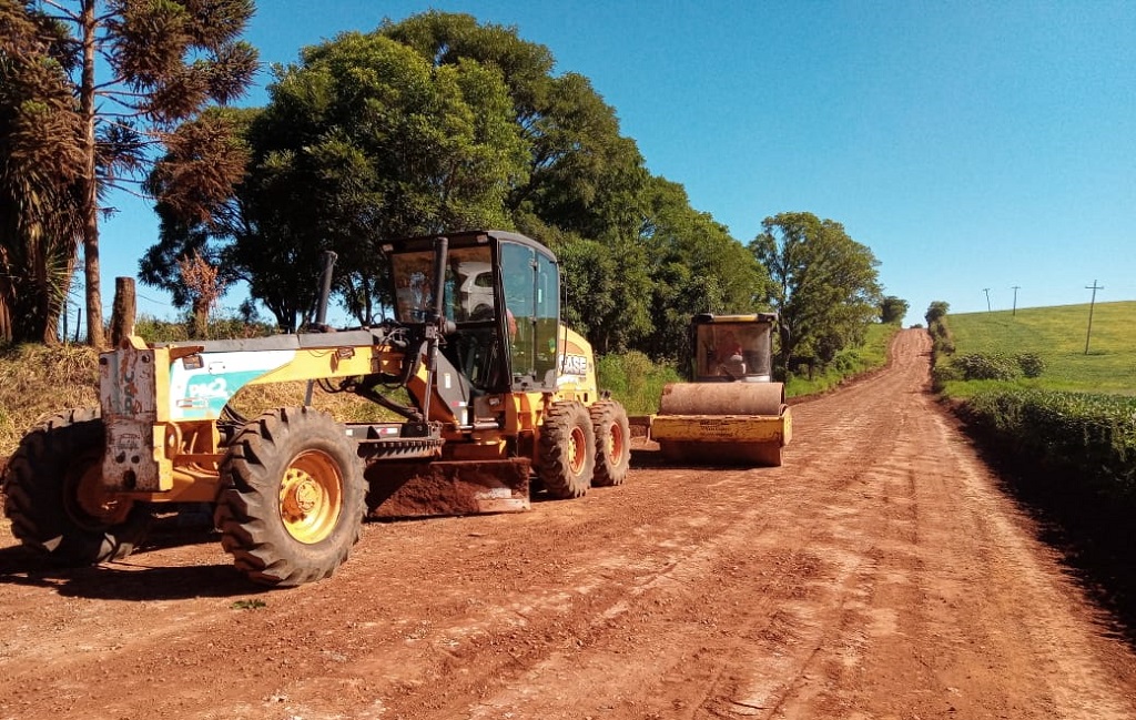Retroescavadeira e motoniveladora trabalham em estrada rural de terra no interior do RS
