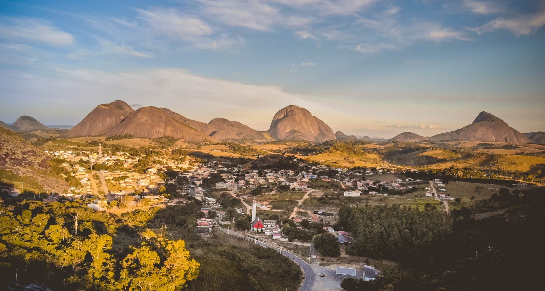 Vista panorâmica de Vila Pavão ES, com área urbana cercada por morros e vegetação ao fundo.