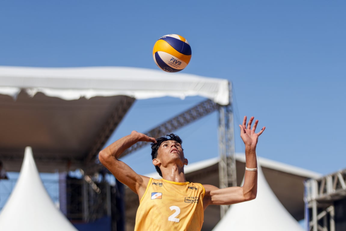 Jovem praticando voleibol, no salto para o saque, durante evento esportivo