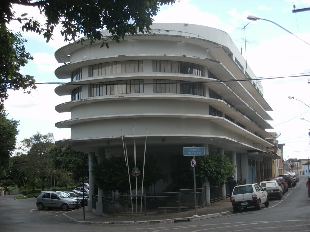 Fachada de prédio legislativo municipal com bandeiras hasteadas, em dia ensolarado
