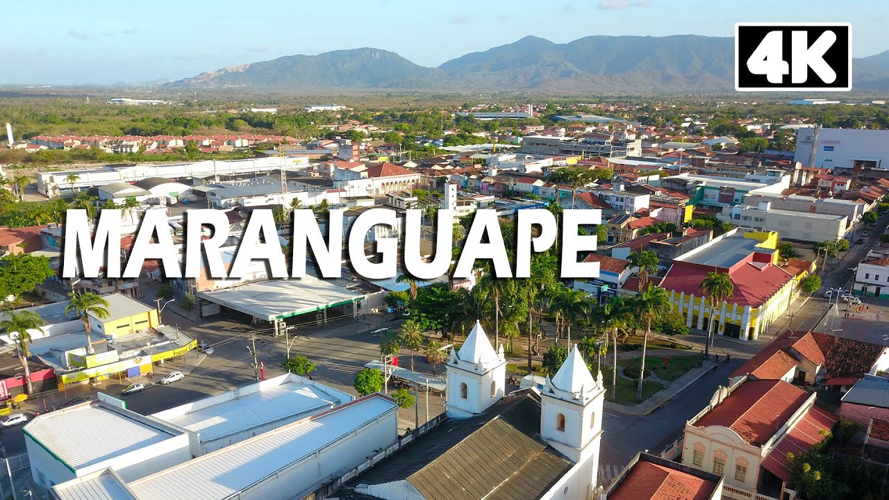 Vista aérea de Maranguape, com a serra ao fundo e a cidade entre vegetação e áreas urbanas, em dia de céu claro