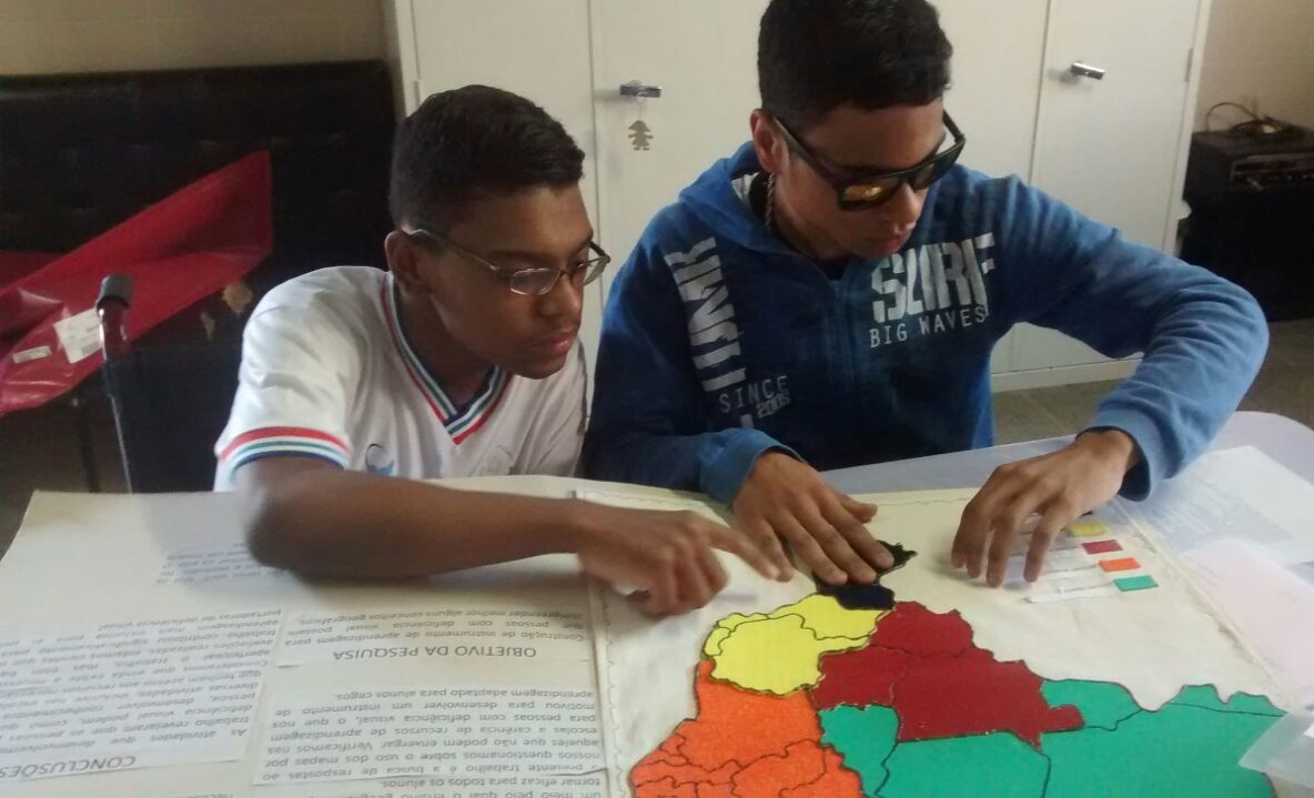 Sala de aula inclusiva com professor utilizando material tátil com aluno com deficiência visual