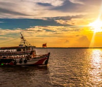 Pôr do sol na Baía do Guajará, com embarcação em destaque e a silhueta urbana de Belém PA ao fundo.