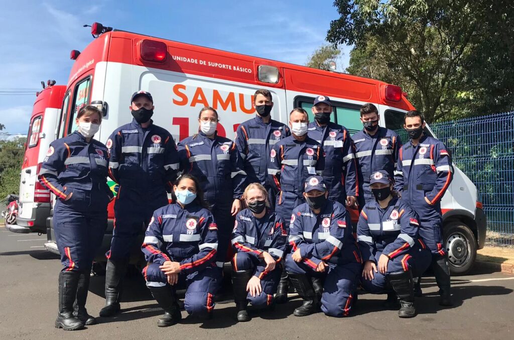 Equipe do SAMU em frente a uma ambulância, em contexto urbano
