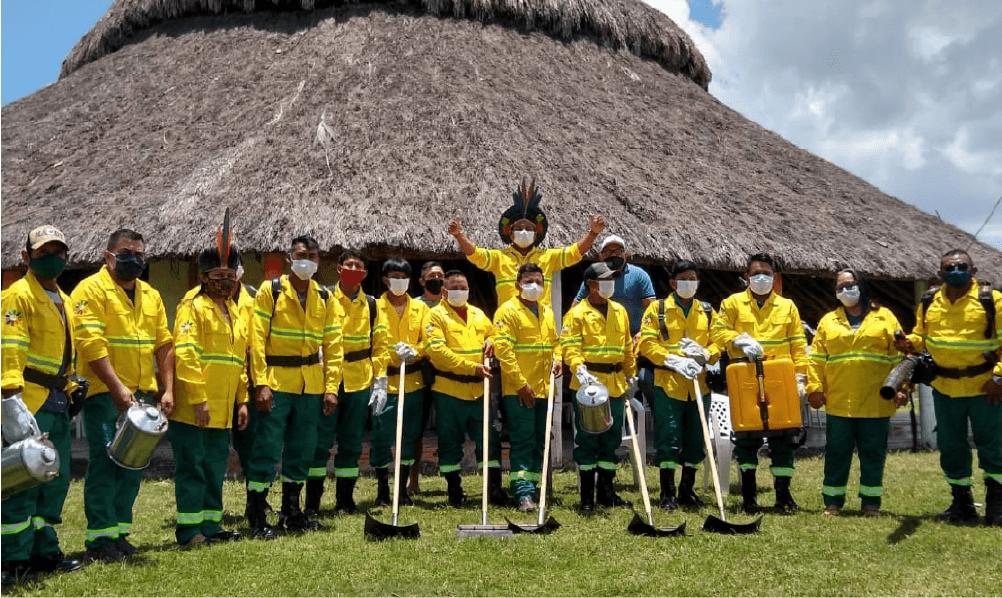 Brigadistas em ação com EPIs e bomba costal em área de vegetação amazônica