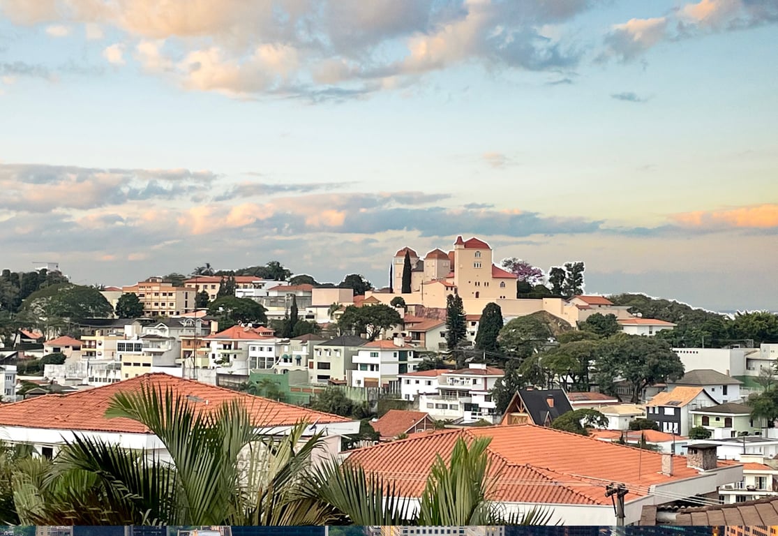 Centro urbano de cidade do interior paulista, com praça arborizada e igreja ao fundo, ao fim da tarde