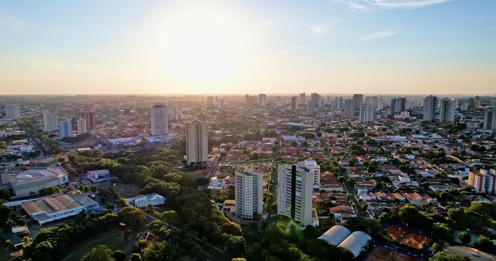 Paisagem urbana de cidade do interior paulista ao entardecer, com áreas verdes e perfil urbano simples, remetendo ao noroeste do estado