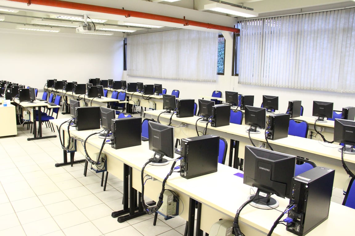 Sala técnica com computadores, alunos e professor em atividade