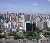 Vista aérea de Porto Alegre ao entardecer, com avenidas movimentadas e a orla do Guaíba ao fundo