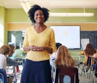 Sala de aula na rede pública, professora à frente e alunos de costas em ambiente iluminado