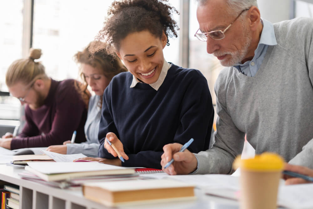 Ambiente acadêmico com professor e alunos em atividade de aprendizagem, material didático sobre a mesa.