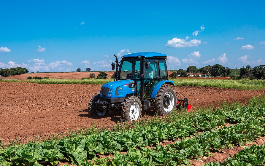 Trator em atividade em área agrícola ao entardecer; composição horizontal, cores quentes.