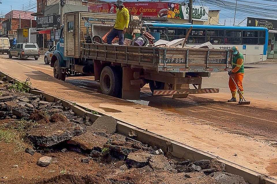 Trabalhadores de serviços urbanos com caminhão e equipamentos em manutenção de via pública, com cones de sinalização.