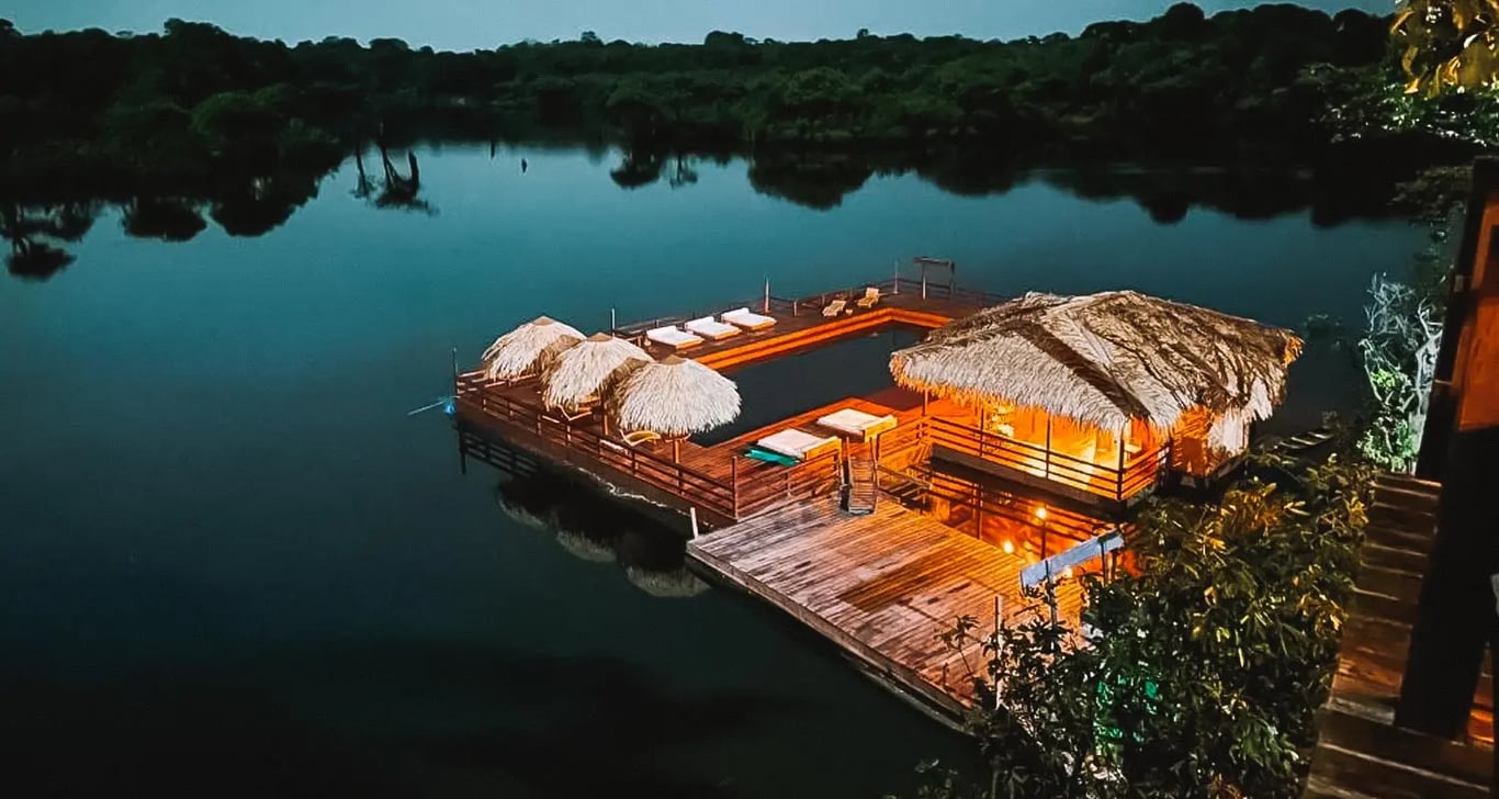Paisagem ribeirinha amazônica ao entardecer, com casas em palafitas e reflexos no rio